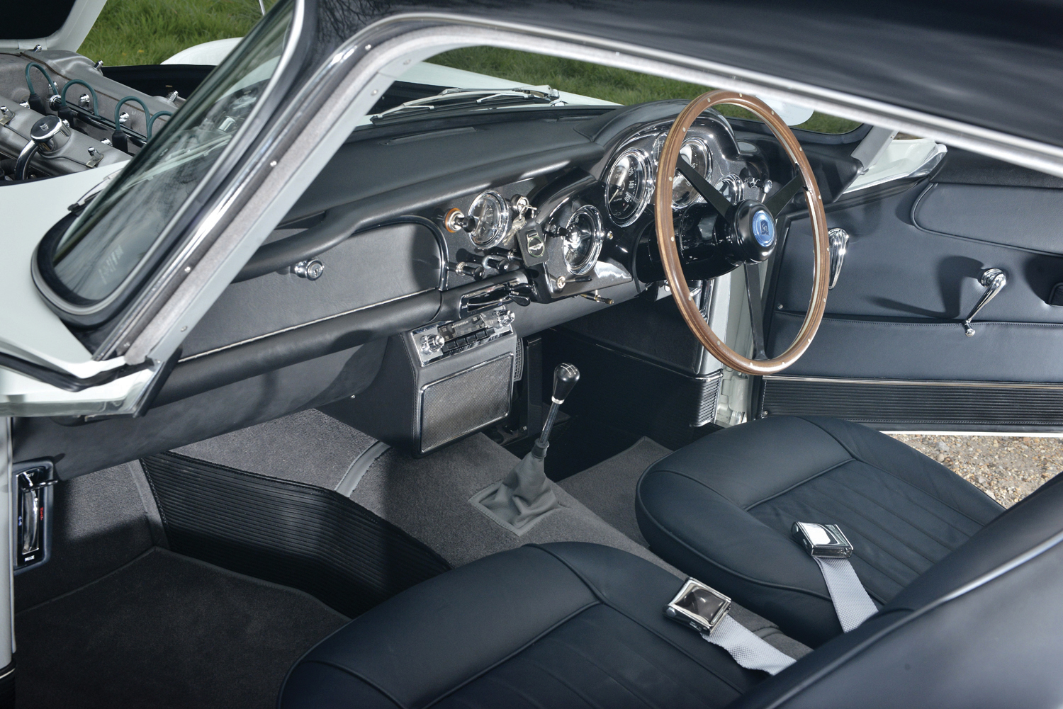 Aston Martin DB4 interior with classic dashboard, analog gauges and wooden steering wheel